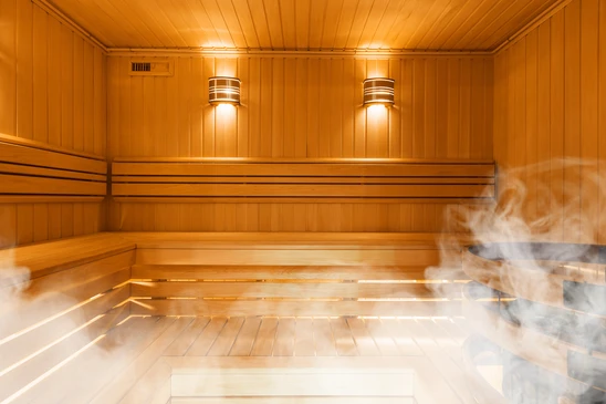 Sauna finlandais en bois clair avec banquettes étagées et vapeur s'échappant du poêle