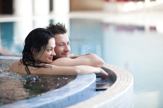 Couple se détendant dans une piscine intérieure, appuyés contre le rebord carrelé, ambiance spa et bien-être