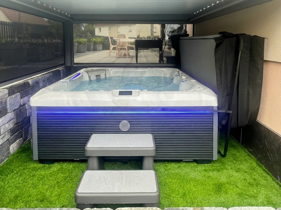 Spa jacuzzi encastré dans un abri fermé avec parois vitrées coulissantes, posé sur gazon synthétique