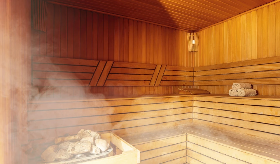 Intérieur de sauna finlandais traditionnel avec banquettes en bois étagées, vapeur visible s'échappant du poêle à pierres volcaniques