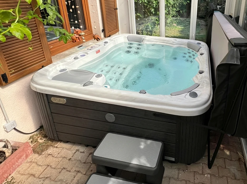 Spa balnéo installé en véranda, coque acrylique blanche marbrée, habillage extérieur en composite imitation bois foncé