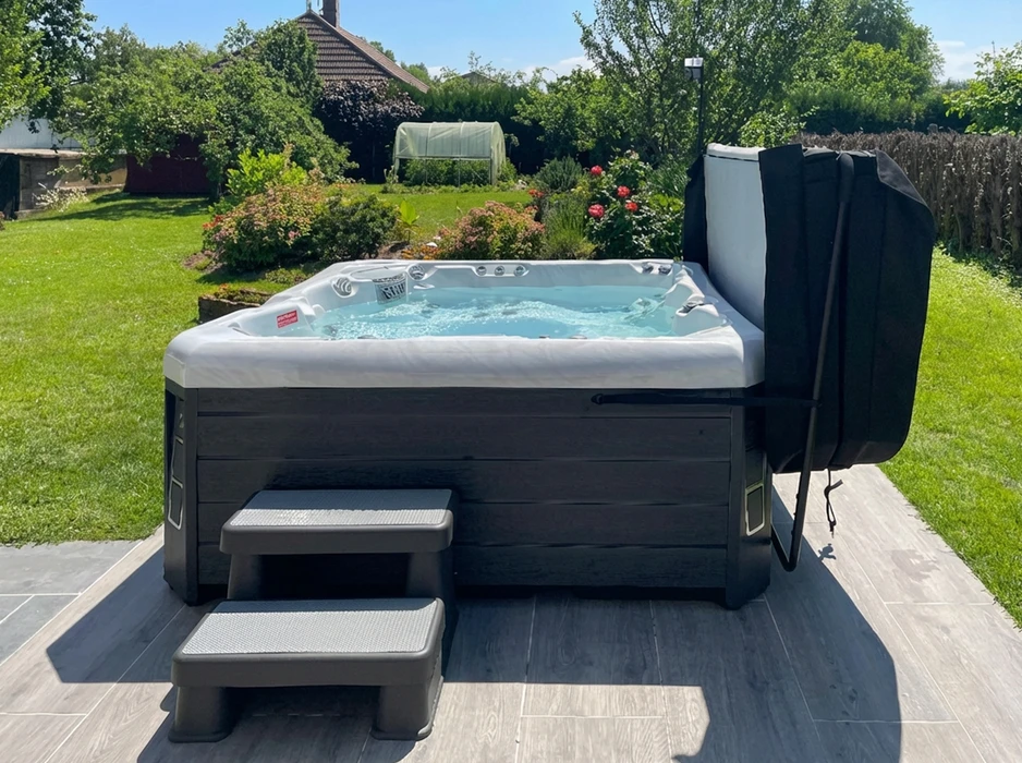 Spa jacuzzi extérieur installé sur une terrasse carrelée dans un jardin verdoyant