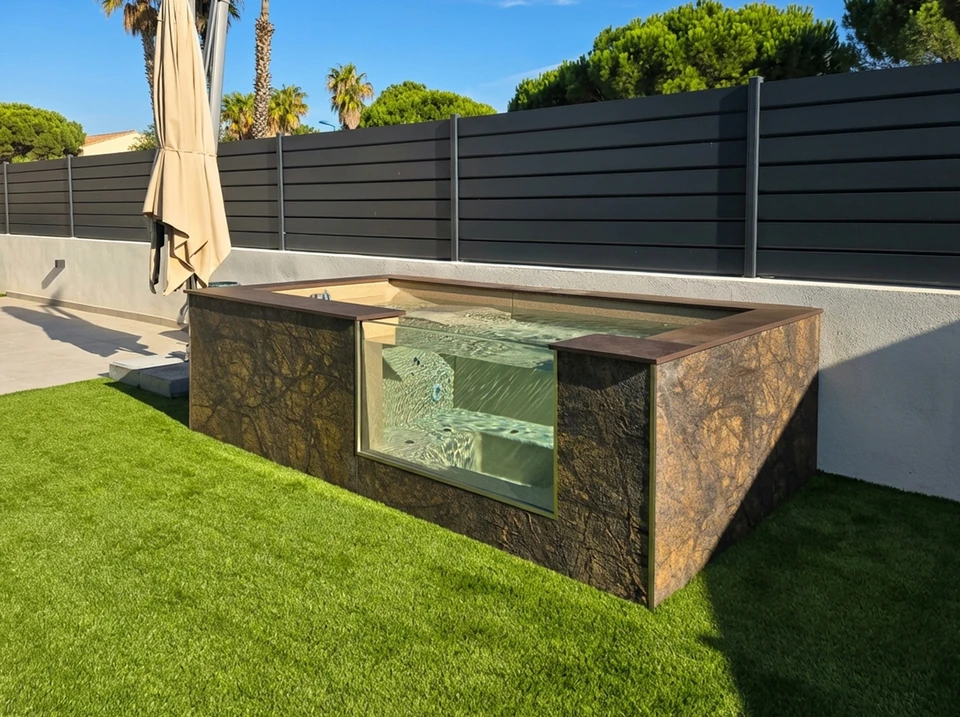 Vue aérienne ou latérale d'une piscine enterrée rectangulaire en béton armé de dimensions modulables, installée dans un jardin résidentiel avec espace vert. La piscine montre clairement les parois en béton, l'intégration harmonieuse au terrain naturel, avec un jardin verdoyant en arrière-plan. L'image doit démontrer l'adaptation du bassin à l'espace disponible et la robustesse de la structure béton.