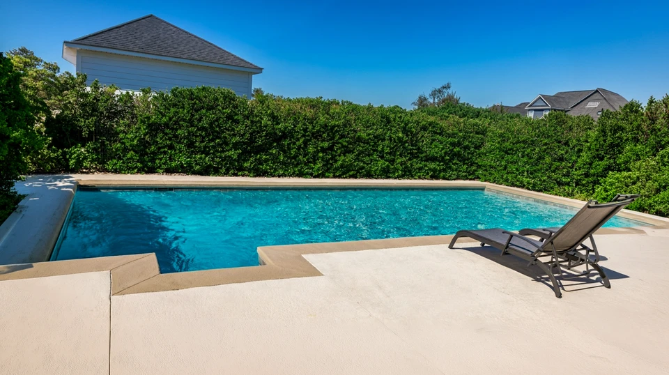Piscine creusée extérieure de forme libre avec eau bleue cristalline, entourée d'une terrasse en pavés de béton beiges disposés en motif courbe