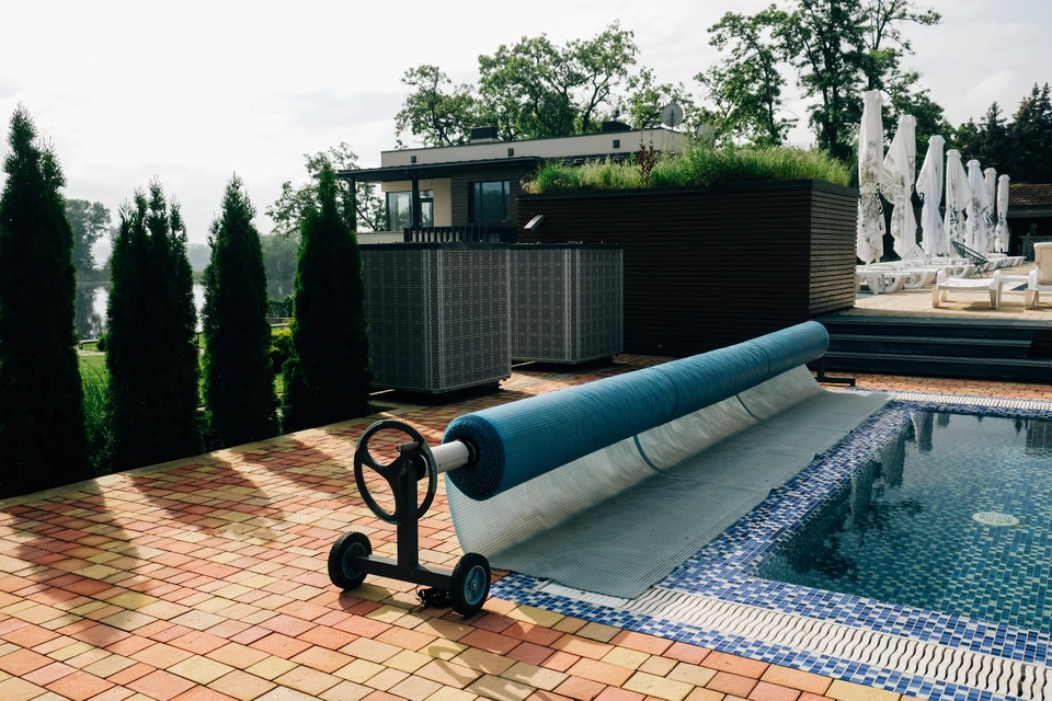 Scène extérieure autour d'une piscine avec enrouleur de bâche automatique installé sur margelles en pierre claire
