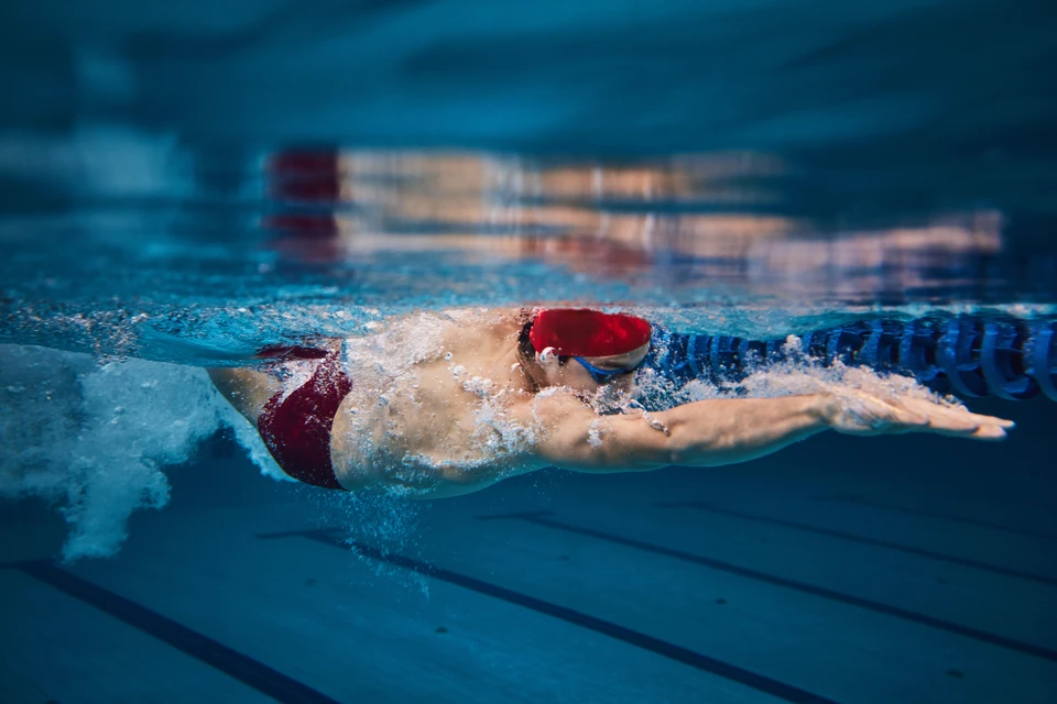 Femme blonde souriante en maillot de bain rouge assise sur transat au bord d'une piscine intérieure moderne