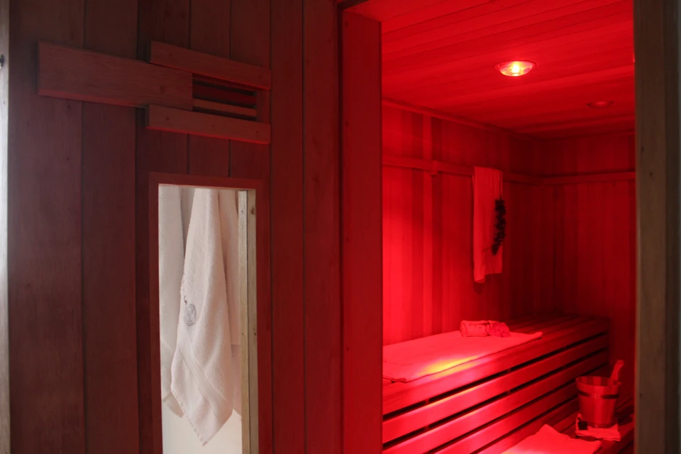 Femme détendue dans un fauteuil de massage électrique noir près d'une baie vitrée, yeux fermés, portant une robe grise